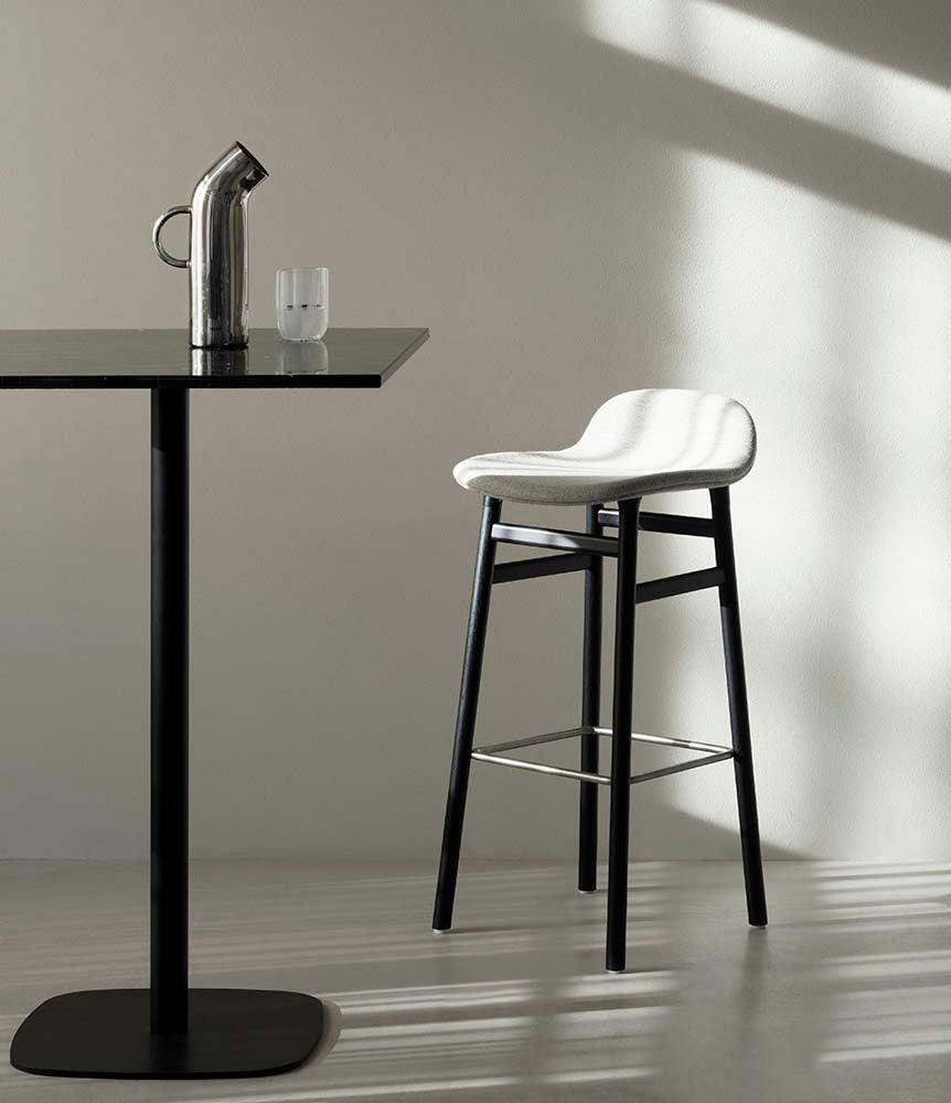 Grijze plastic barkruk met zwarte gelakte houten poten en metalen voetensteun, modern design.
