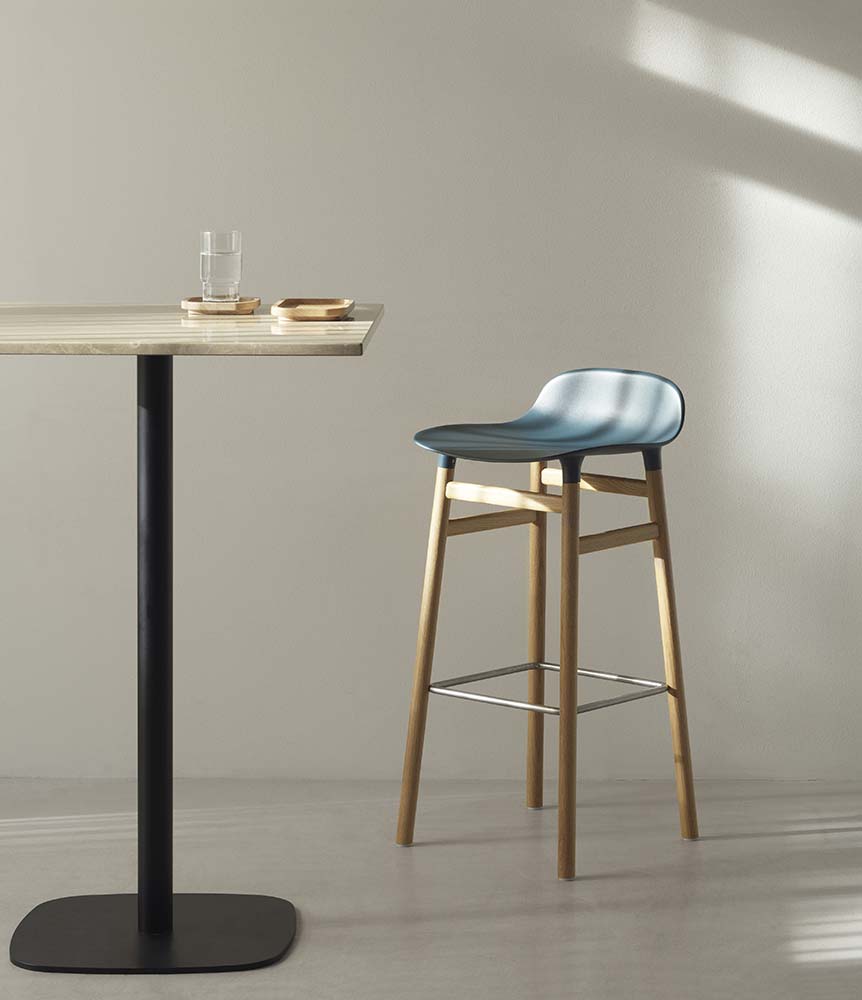 Zwarte plastic barkruk met eikenhouten poten en metalen voetensteun, modern design. Normann Copenhagen.